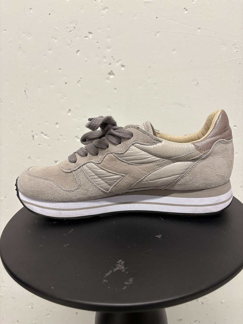 Grauer Sneaker, seitliche Ansicht auf einem runden, schwarzen Sockel. Sportliche Schuhmode.