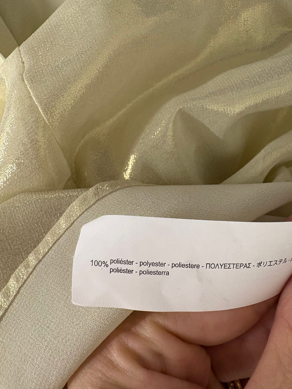 Miniaturbild: Nahaufnahme eines goldfarbenen Stoffes mit Text: 100% Polyester.