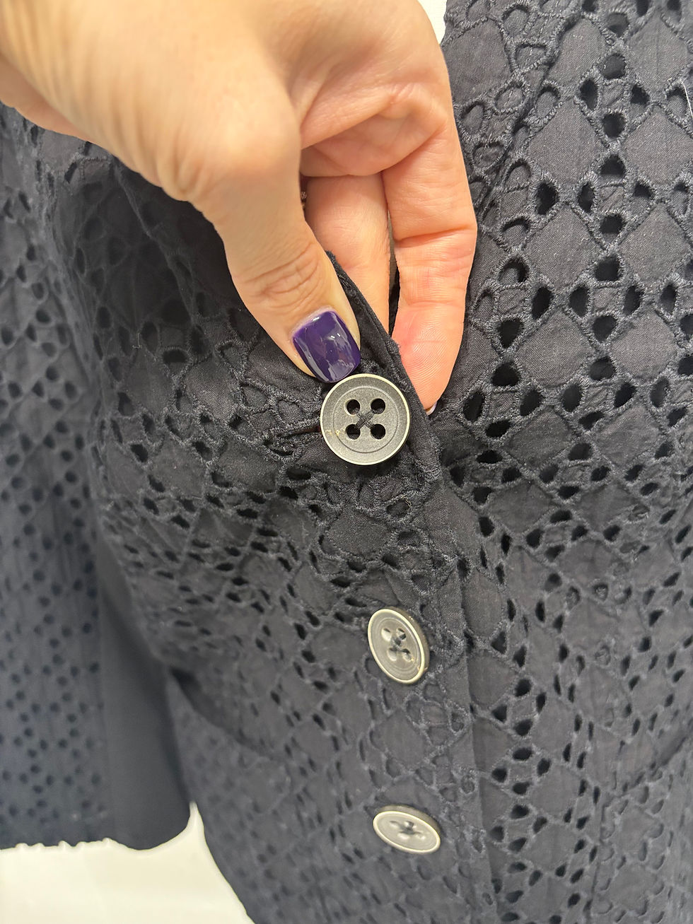 Miniaturbild: Hand drückt Knopf an dunkelblauer Bluse mit Lochmuster. Nahaufnahme von Details.