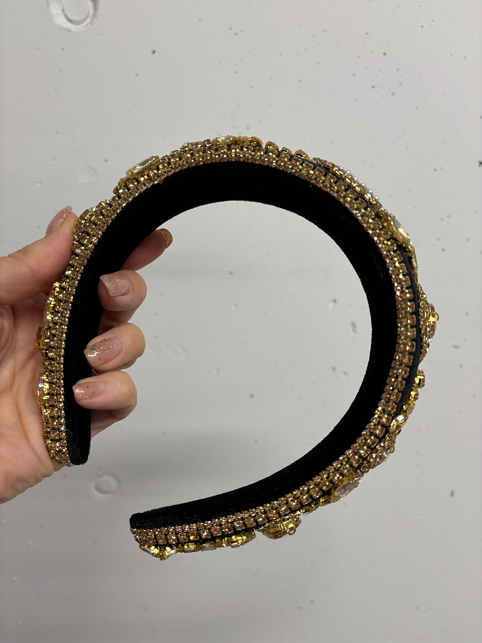 Miniaturbild: Hand holding a gold-colored headband with lots of embedded rhinestones