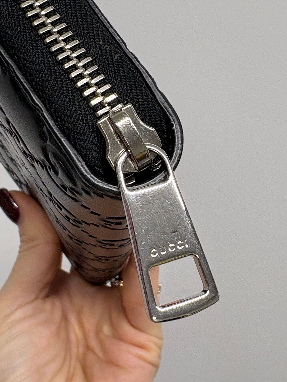 Miniaturbild: Schwarze Gucci-Geldbörse mit Reißverschluss und eingraviertem Gucci-Logo, Nahaufnahme.