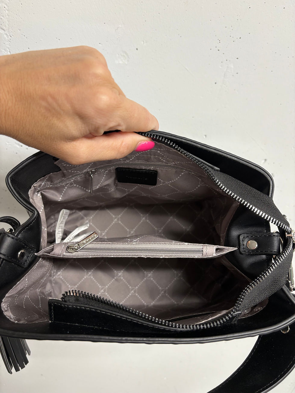 Miniaturbild: Schwarze Handtasche, offene Reißverschlüsse, der Innenraum sichtbar, Details in der Tasche. 