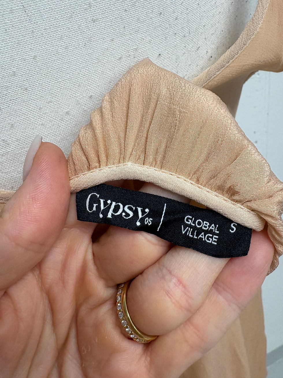 Miniaturbild: Gypsy 95 label reads GLOBAL S VILLAGE on beige clothing close up.