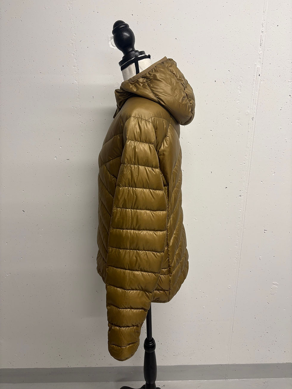 Goldene Steppjacke mit Kapuze an einer Büste vor grauem Hintergrund.