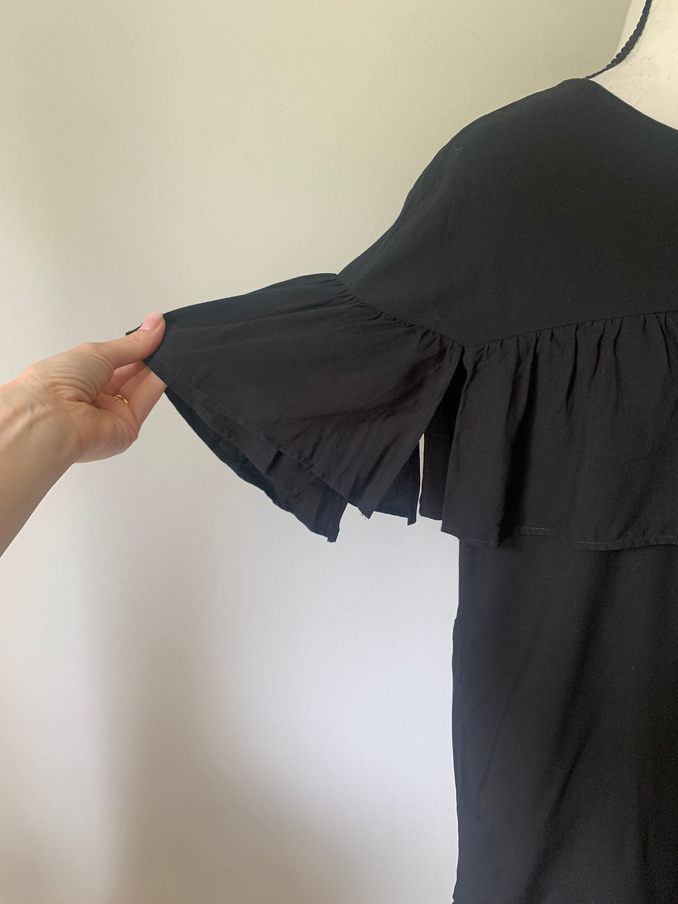 Miniaturbild: Schwarzes Kleid mit Rüschenärmel, Detailaufnahme einer Hand, die den Stoff berührt.