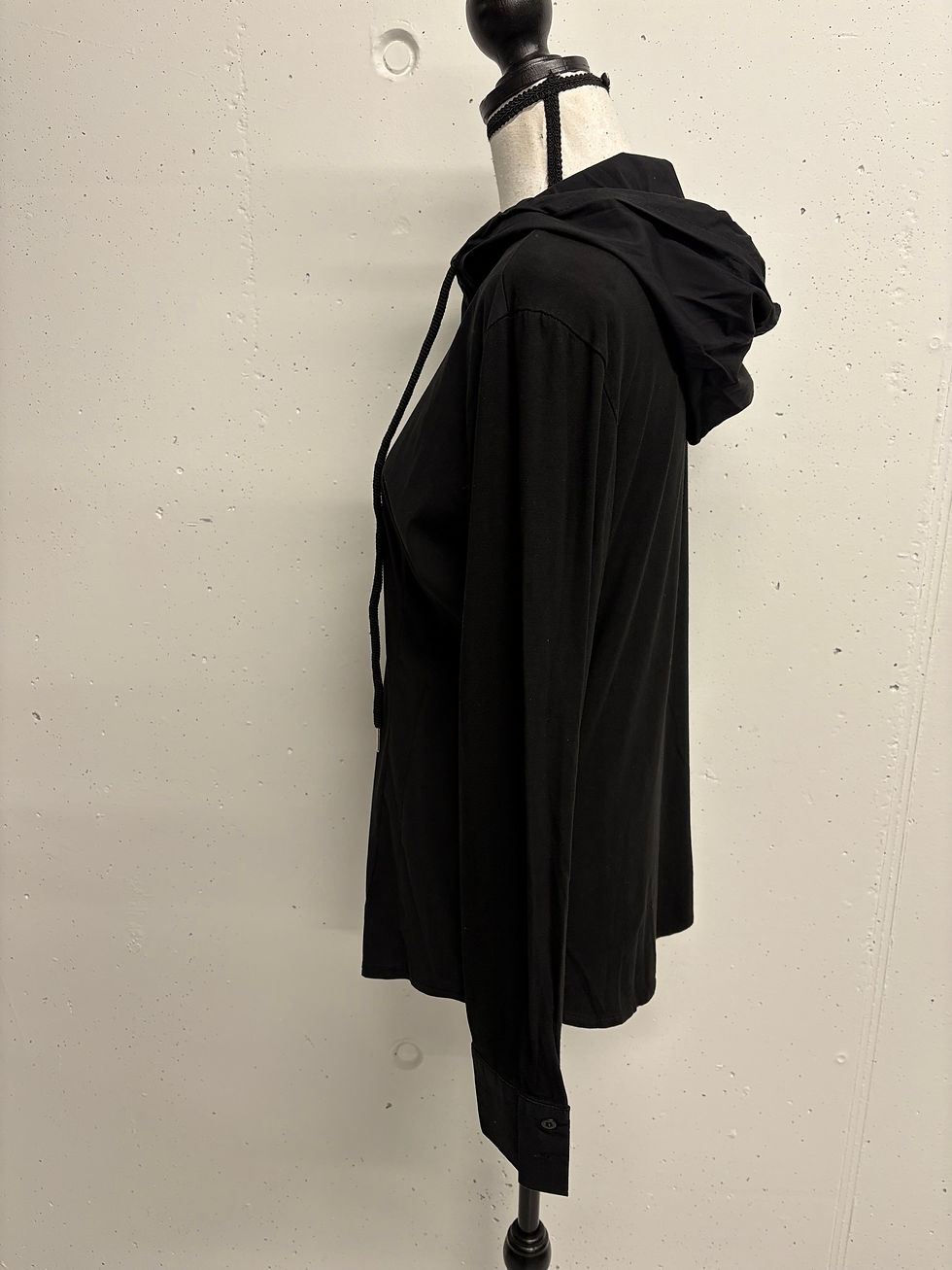 Miniaturbild: Schwarzer Kapuzenpullover auf einer Schaufensterpuppe in einem Verkaufsraum.