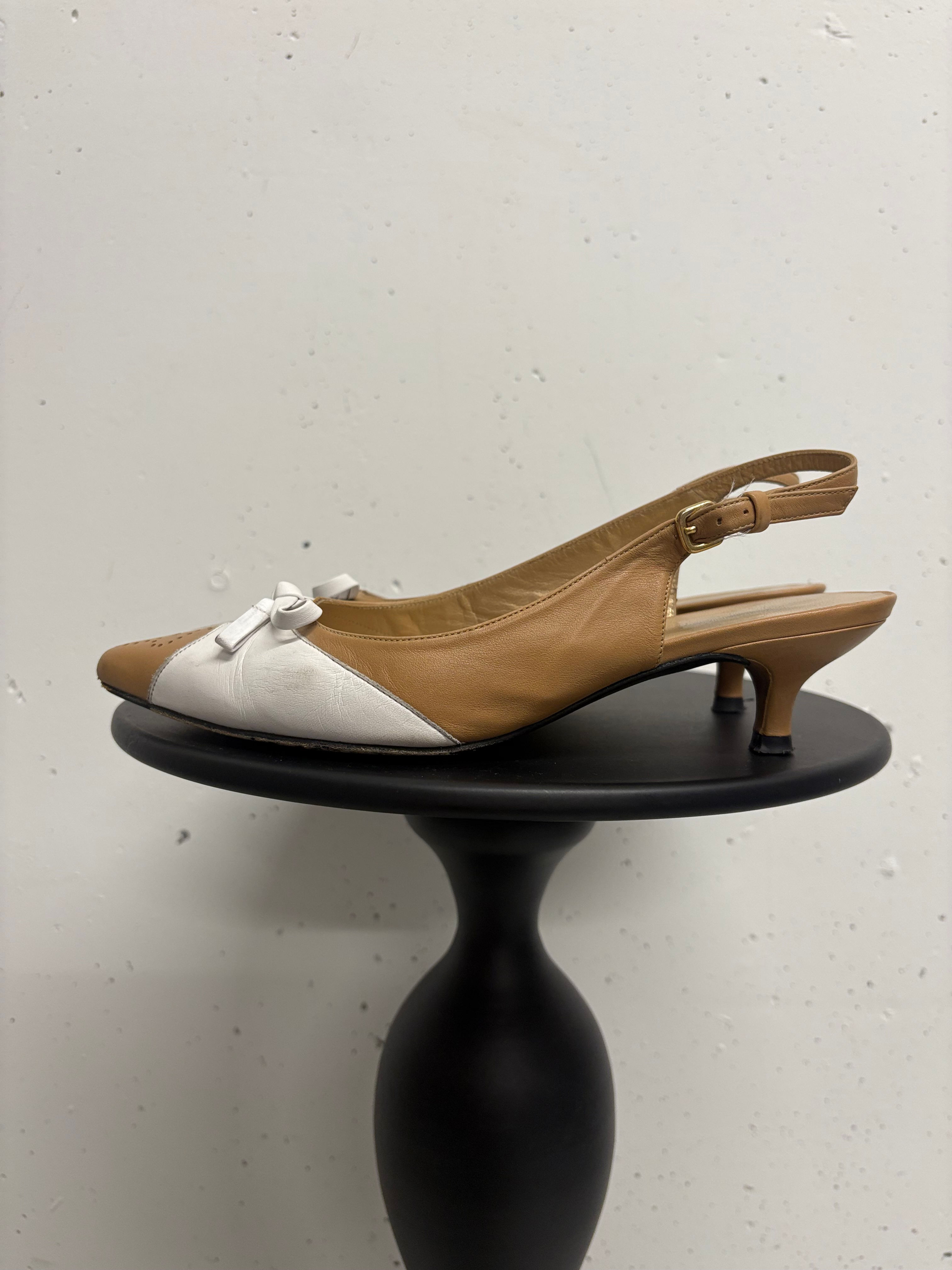 Braune und weiße Damenschuhe mit Schleife stehen auf einem kleinen Tisch.