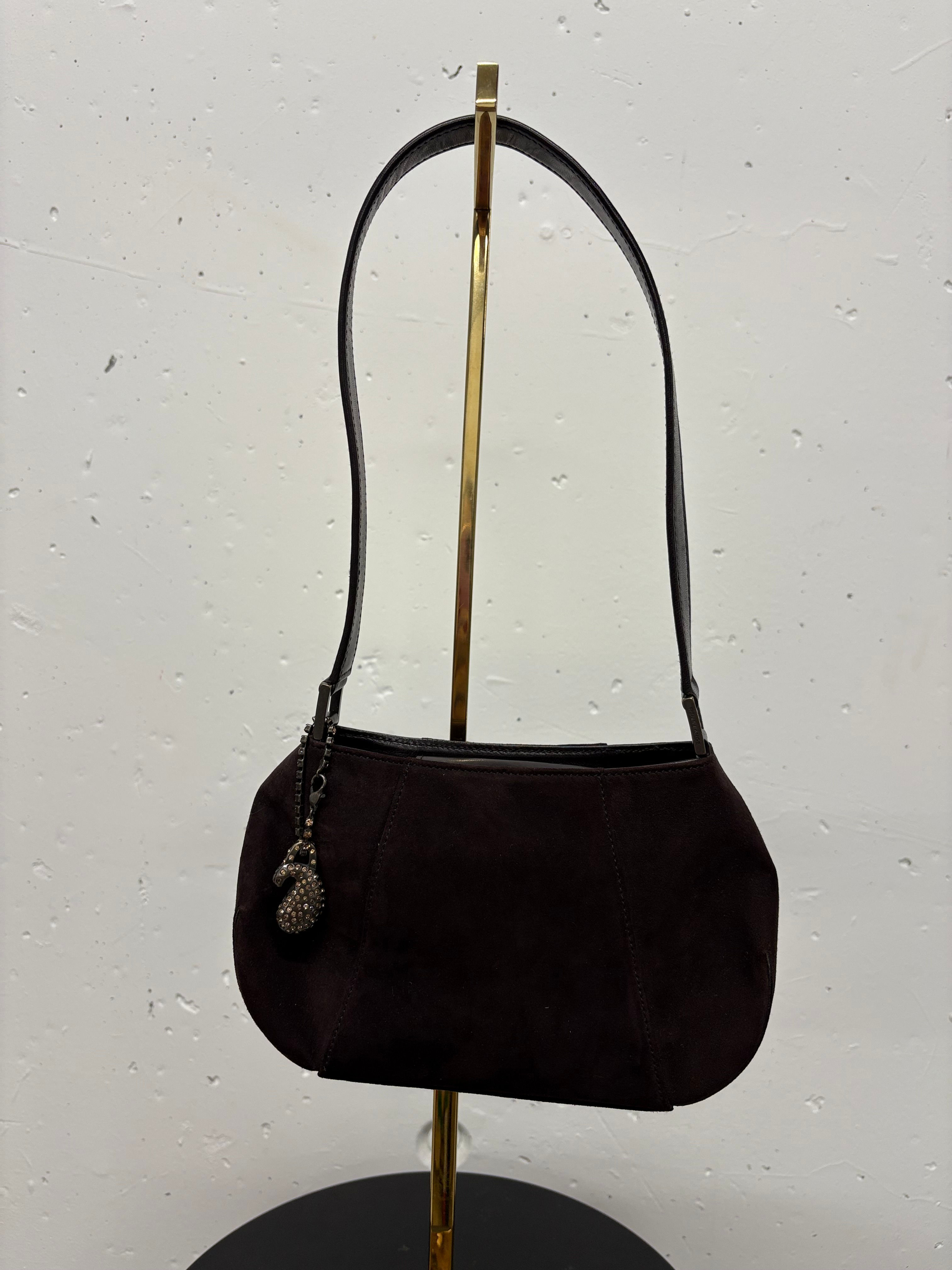 Dunkelbraune Wildleder-Handtasche, Umhängetasche mit Anhänger, vor hellem Hintergrund.