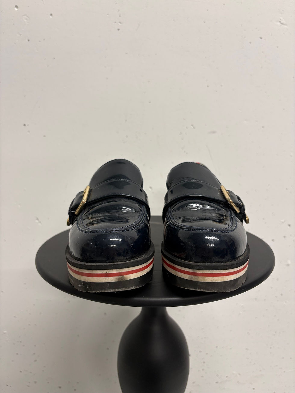 Miniaturbild: Schwarze Lacklederschuhe, goldene Schnallen, sitzen auf einem schwarzen Tisch vor Weiß.