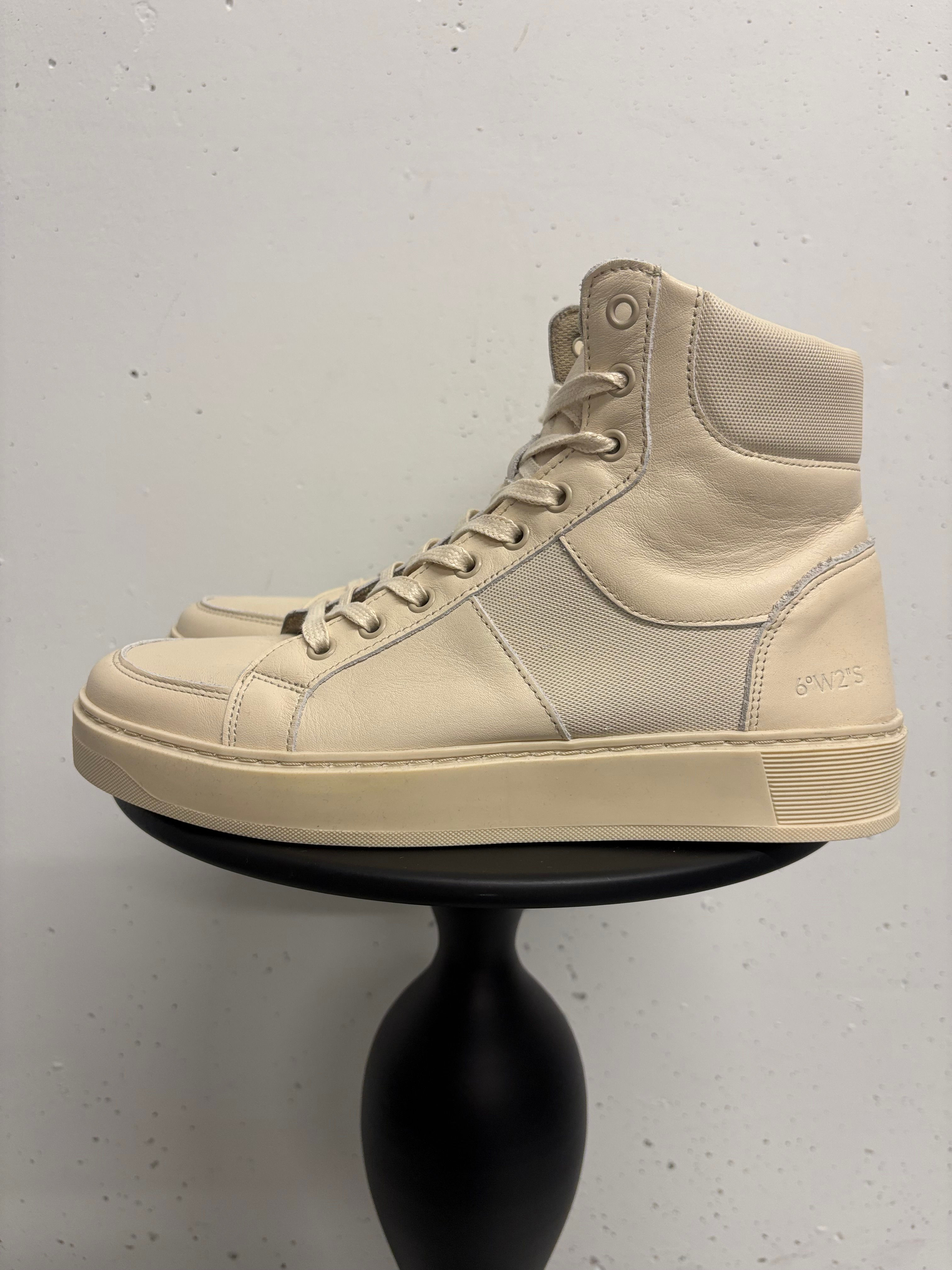 Hochwertige cremefarbene Leder-Sneakers auf einem kleinen schwarzen Hocker im Studio