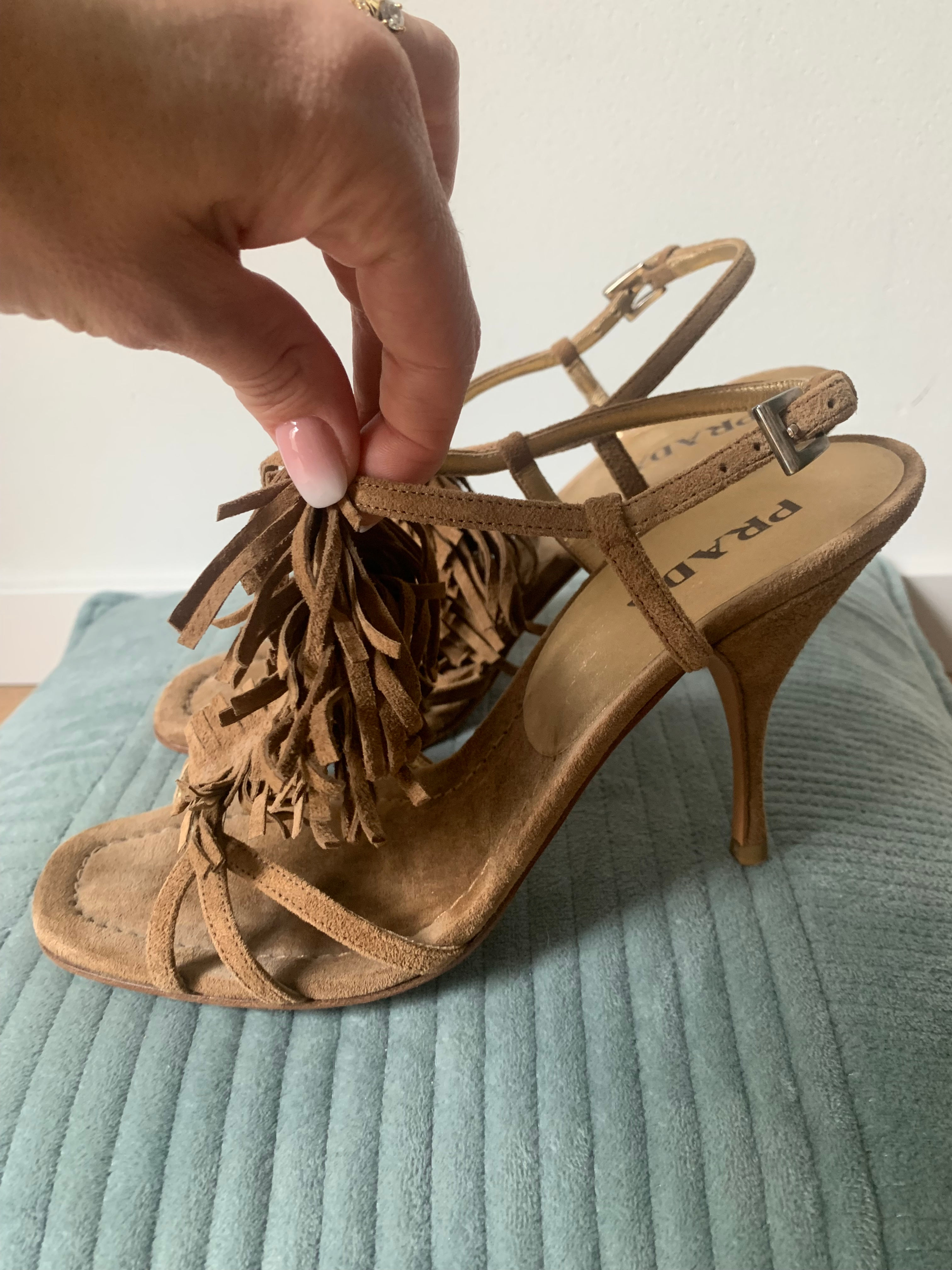 Frau hält beiges Prada Absatzschuh mit Fransen auf blauem Kissen