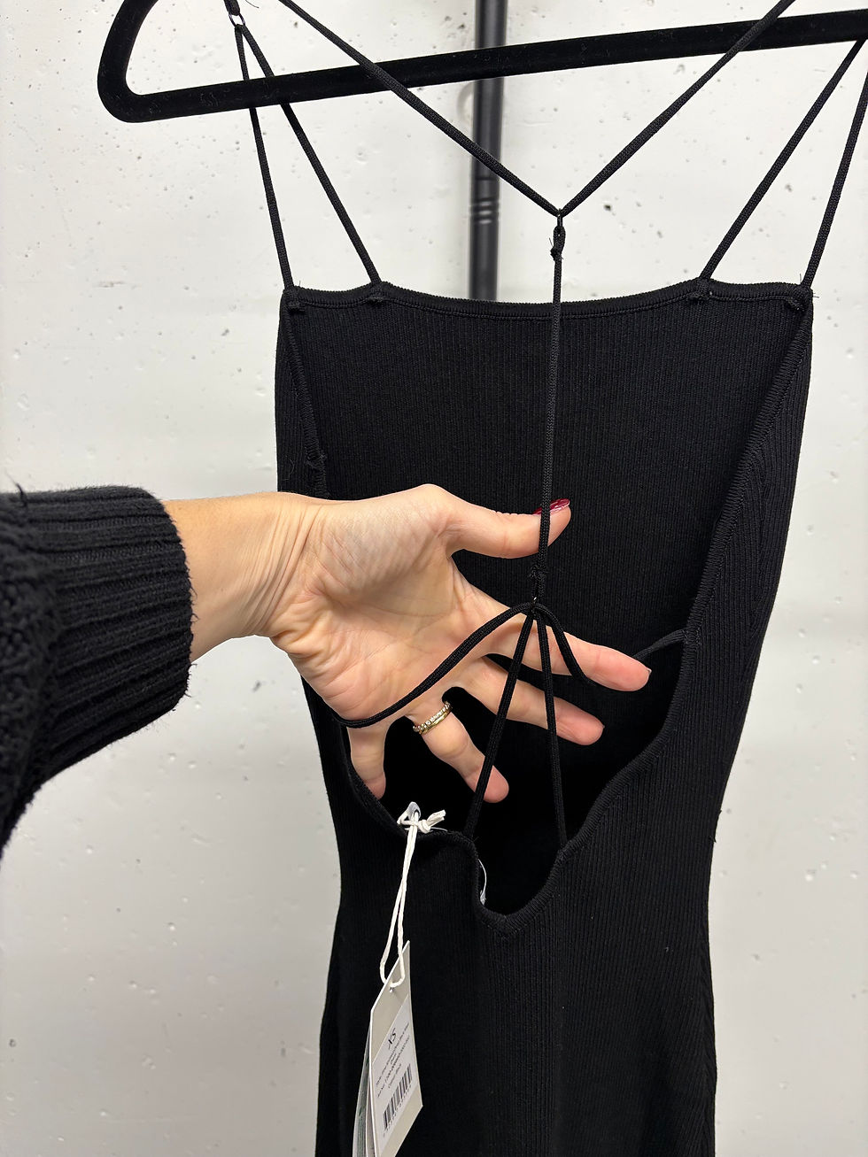 Miniaturbild: Schwarz rückenfreies Kleid mit Spaghettiträgern, Person berührt Kleidung Detail