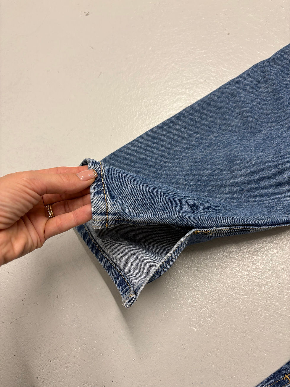 Miniaturbild: Hand hält Denim-Jeans-Saum auf weißem Hintergrund, Detailaufnahme von Jeans.