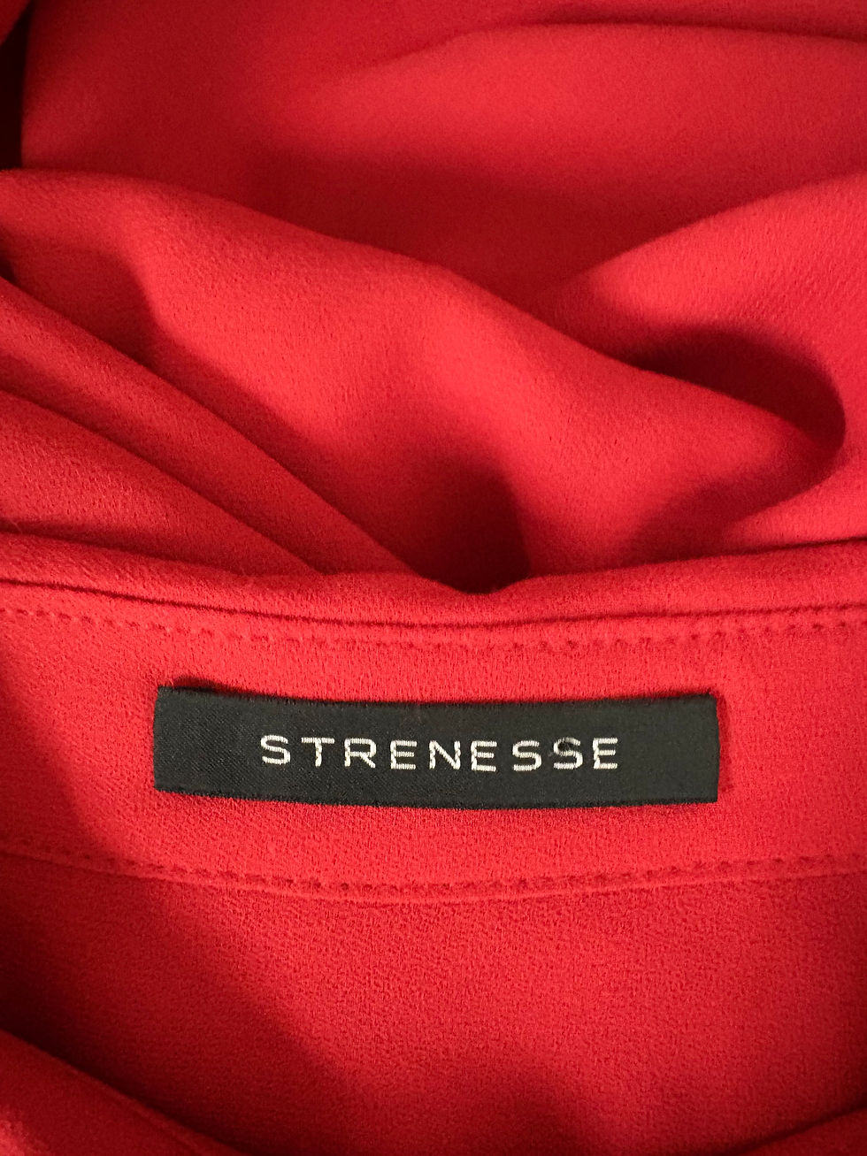Miniaturbild: Nahaufnahme eines roten Hemdes mit dem Label STRENESSE im Fokus.