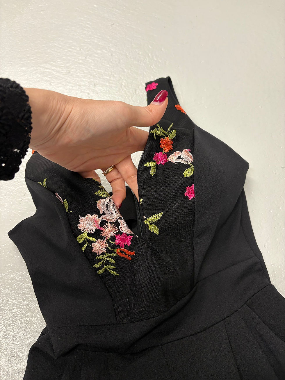 Miniaturbild: Schwarzes Kleid mit floralen Stickereien. Eine Hand öffnet das Dekolleté Detail.