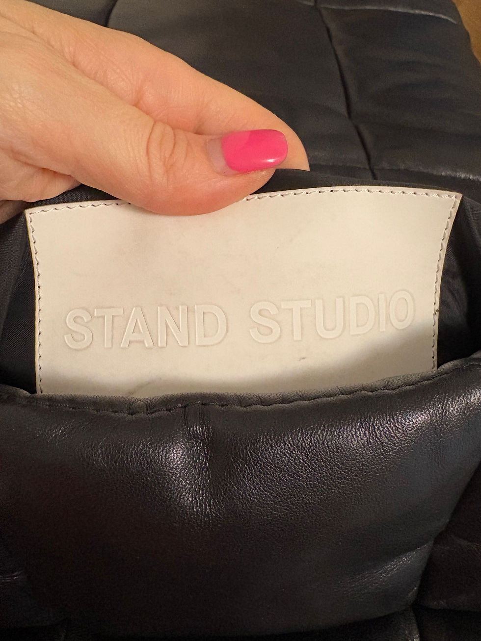 Miniaturbild: Hand holds a black jacket with “STAND STUDIO” label inside.