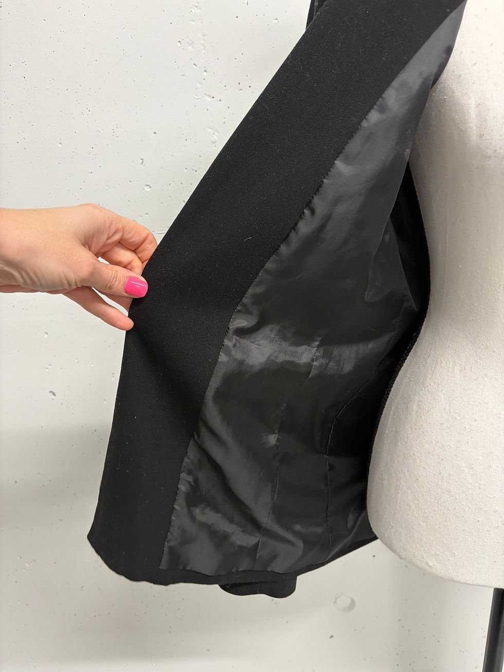 Miniaturbild: Hand zeigt Innenseite einer schwarzen Jacke, auf einem Schaufensterpuppenkörper.