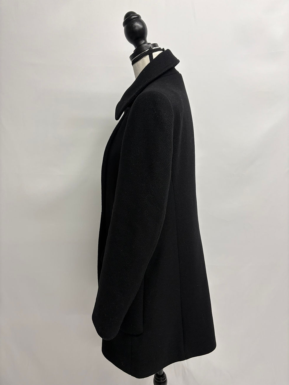 Schwarzer Mantel auf einer Büste, elegant, schlicht gehalten, aus Wolle.