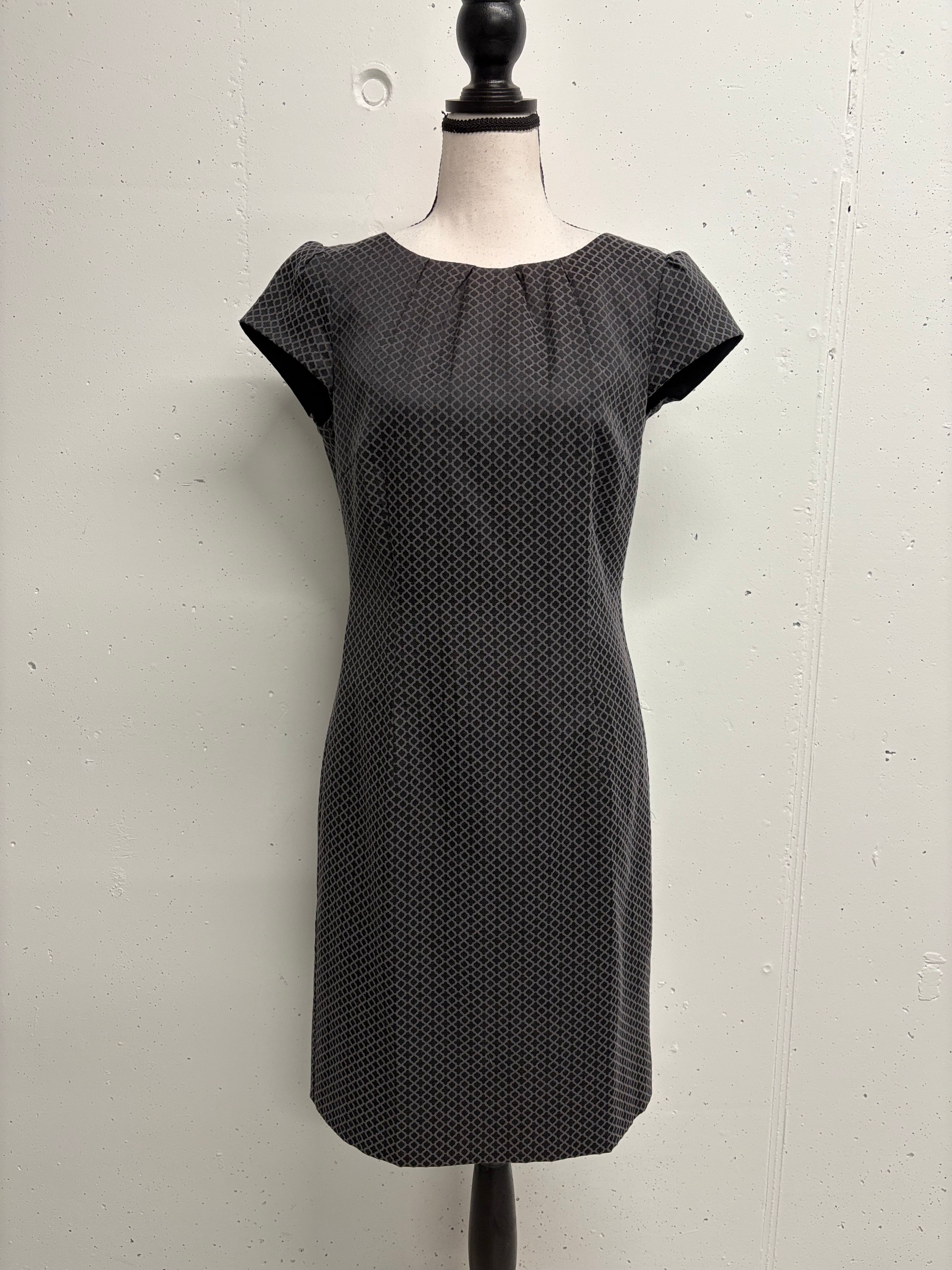 Dunkelgraues Kleid mit kurzen Ärmeln und gepunktetem Muster vor weißem Hintergrund.