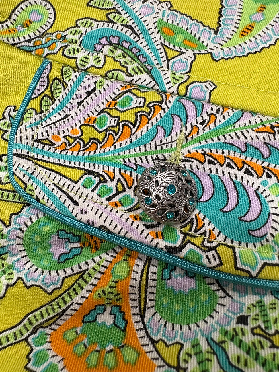 Miniaturbild: Nahaufnahme einer bunten Stoffhose mit türkisfarbenem Muster und silbernem Knopf.