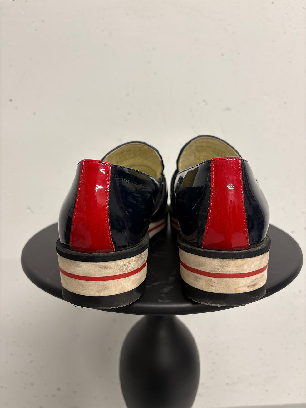 Miniaturbild: Paar schwarze Schuhe mit rotem Detail auf einem kleinen Tisch. 
