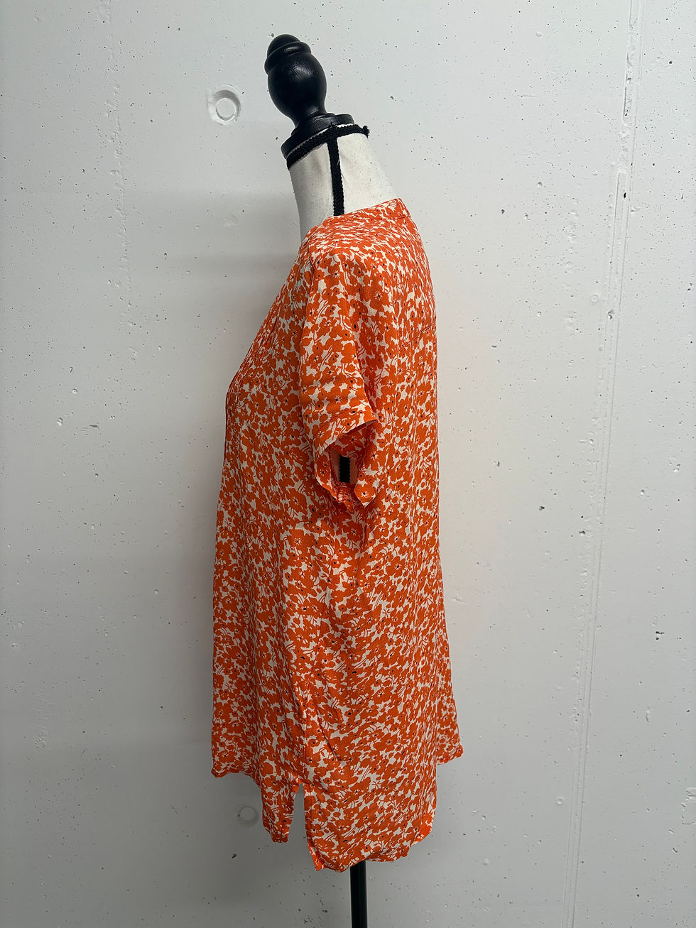 Miniaturbild: Orange-weißes Kurzarmshirt mit Blumendruck, Blick auf die Seite, vor weißem Hintergrund.