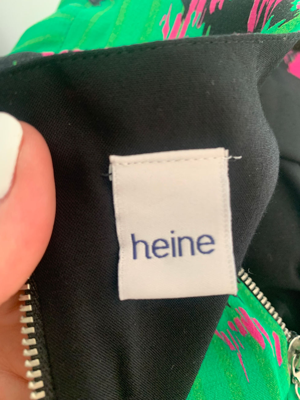 Miniaturbild: White label with heine text, black and green background clothing detail shot.