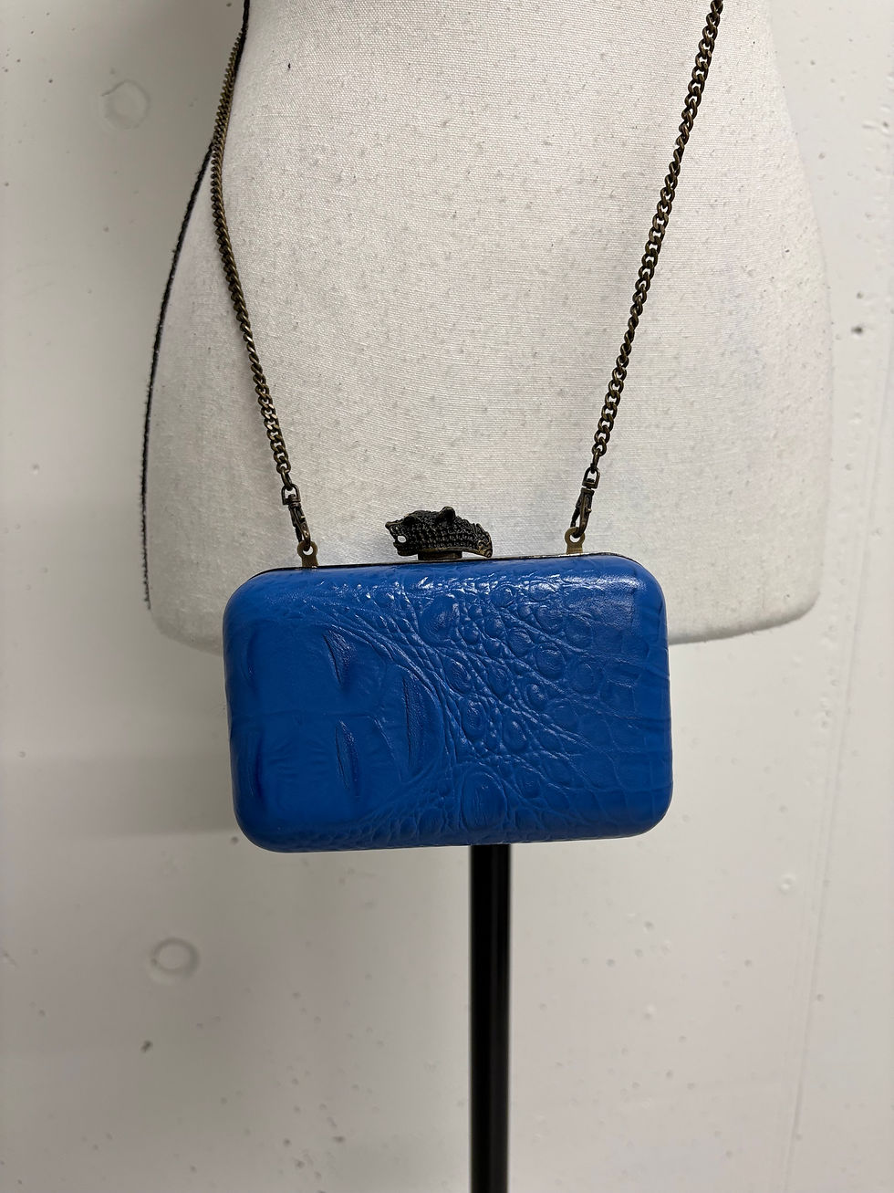 Miniaturbild: Blaue Clutch-Tasche mit Kettenriemen am Schaufensterpuppen-Oberkörper, Nahaufnahme.