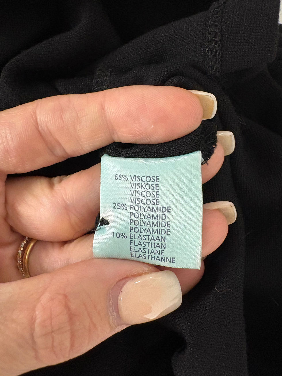 Miniaturbild: Hand hält Etikett mit Text: VISCOSE, POLYAMIDE, ELASTAAN, und weitere Hinweise.