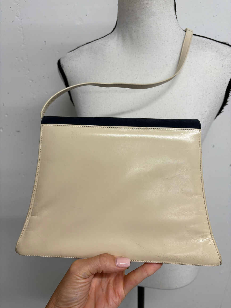 Miniaturbild: Cremefarbene Handtasche mit schwarzem Akzent, Detailaufnahme vor Mode-Büste.