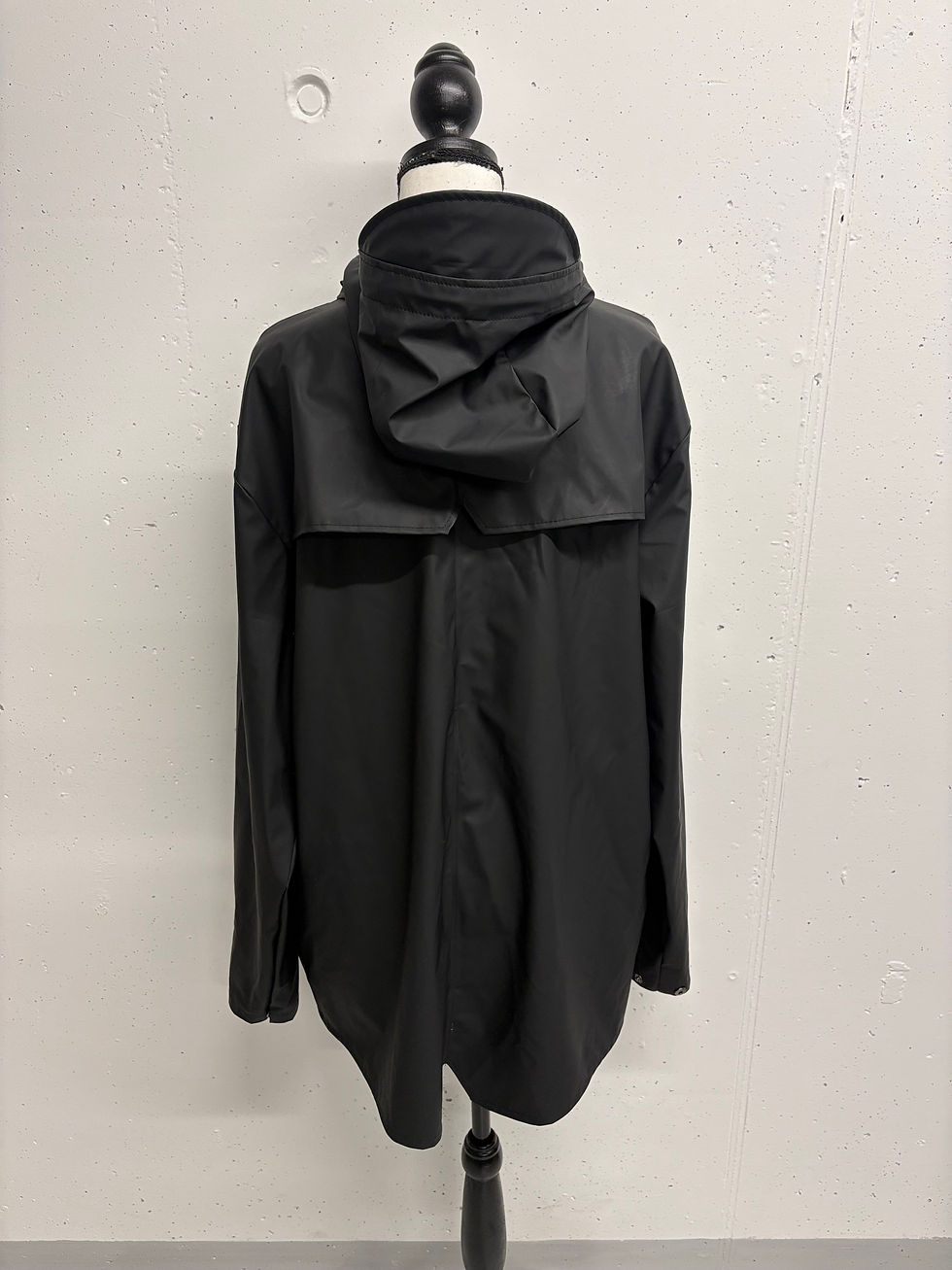 Miniaturbild: Schwarze Jacke mit Kapuze auf einem Kleiderbügel, Rückansicht, Detailaufnahme.
