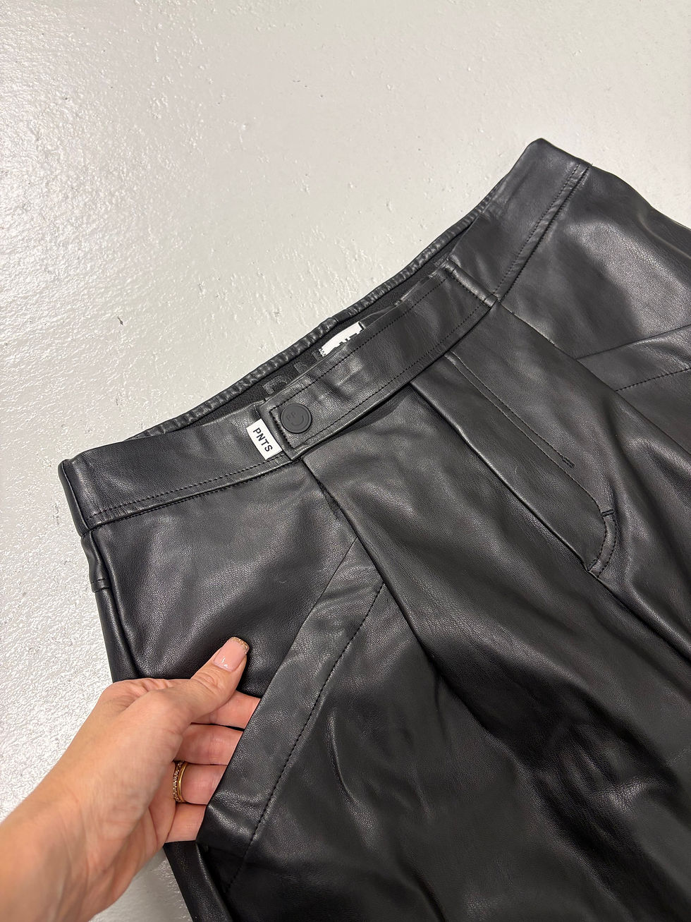 Miniaturbild: Schwarze Lederhose Detailaufnahme, Knopf und Label sichtbar, in stylischem Ambiente, Nahaufnahme.