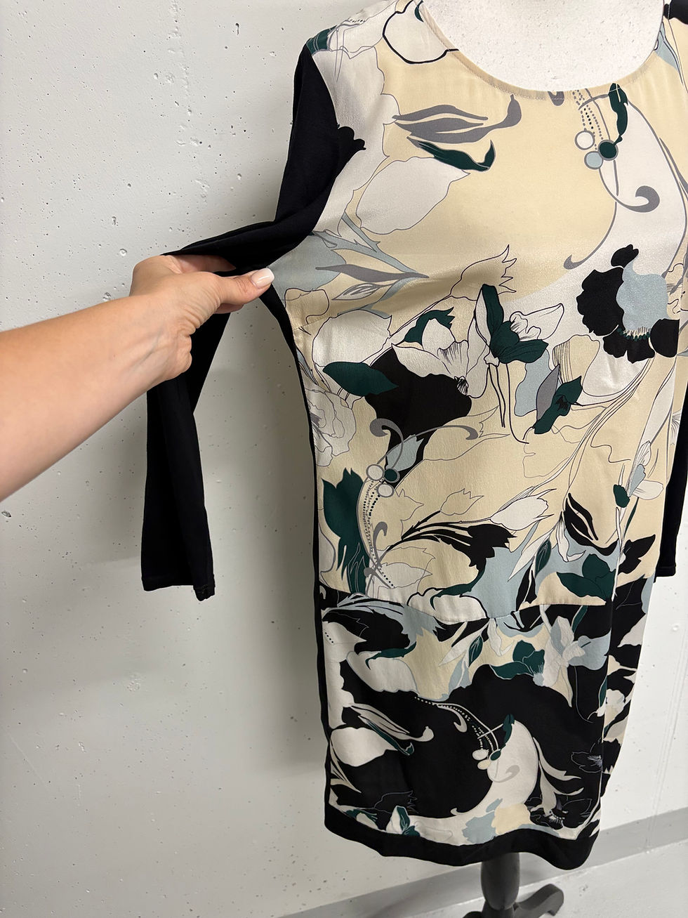 Miniaturbild: Frau zeigt ein Kleid mit floralem Muster und schwarzen Ärmeln, nahaufnahme.