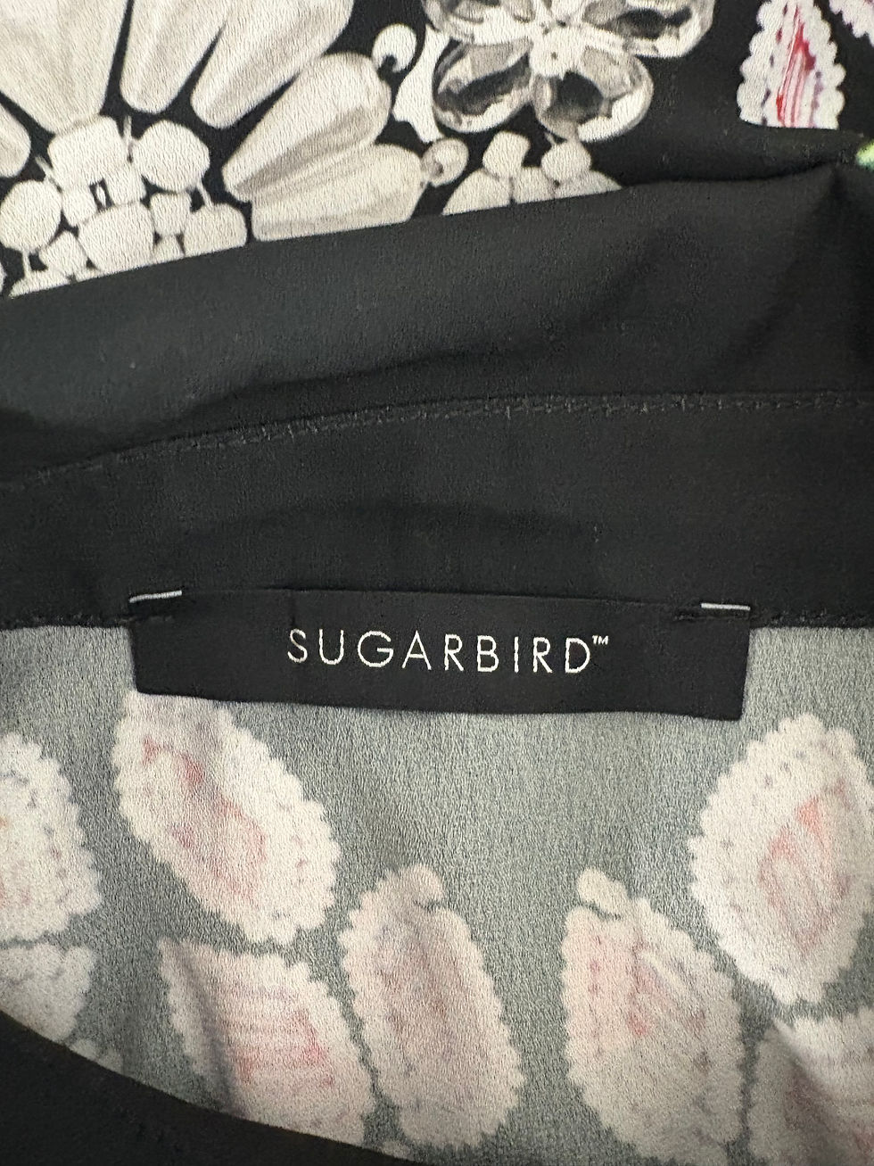 Miniaturbild: SUGARBIRD label on a black shirt with floral pattern close up.