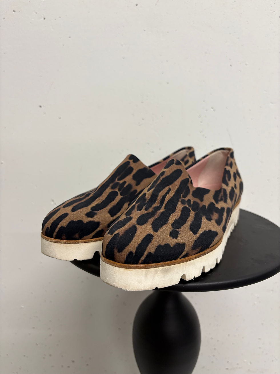 Paar Leoparden-Slipper auf einem schwarzen Tisch vor einer weißen Wand.