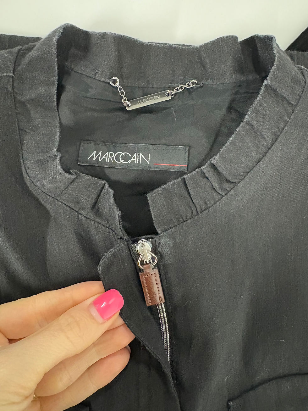 Miniaturbild: Schwarze Jacke mit MARCCAIN-Logo und Reißverschluss, Nahaufnahme einer Hand