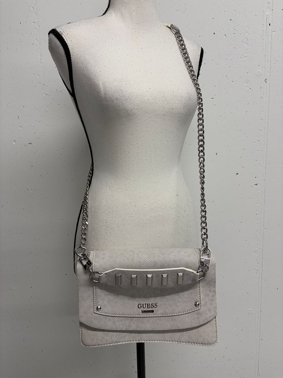 Miniaturbild: Graue Guess Handtasche mit Kette, an einem Schaufensterpuppenkörper präsentiert.