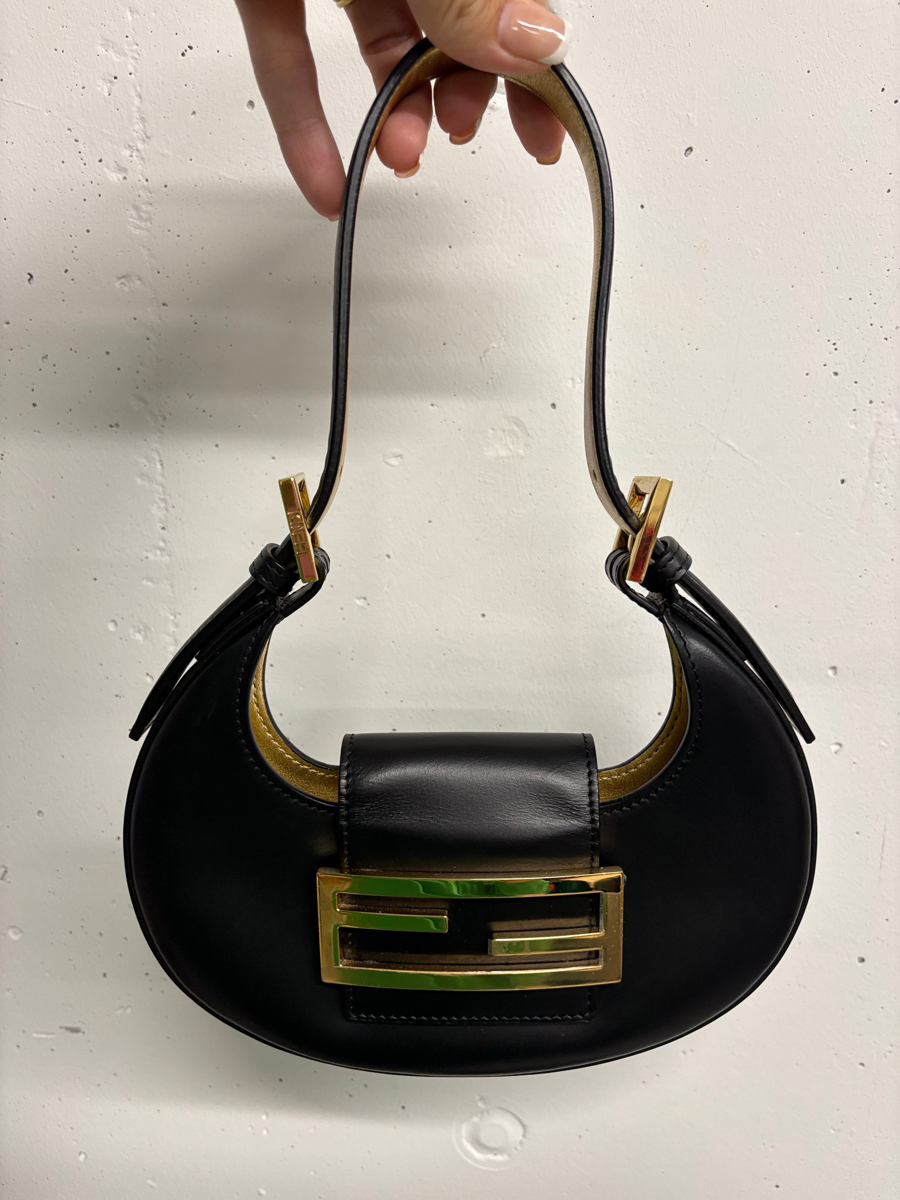 Schwarze Fendi-Handtasche mit goldenem Verschluss und Haltegriff, Nahaufnahme, gehalten.