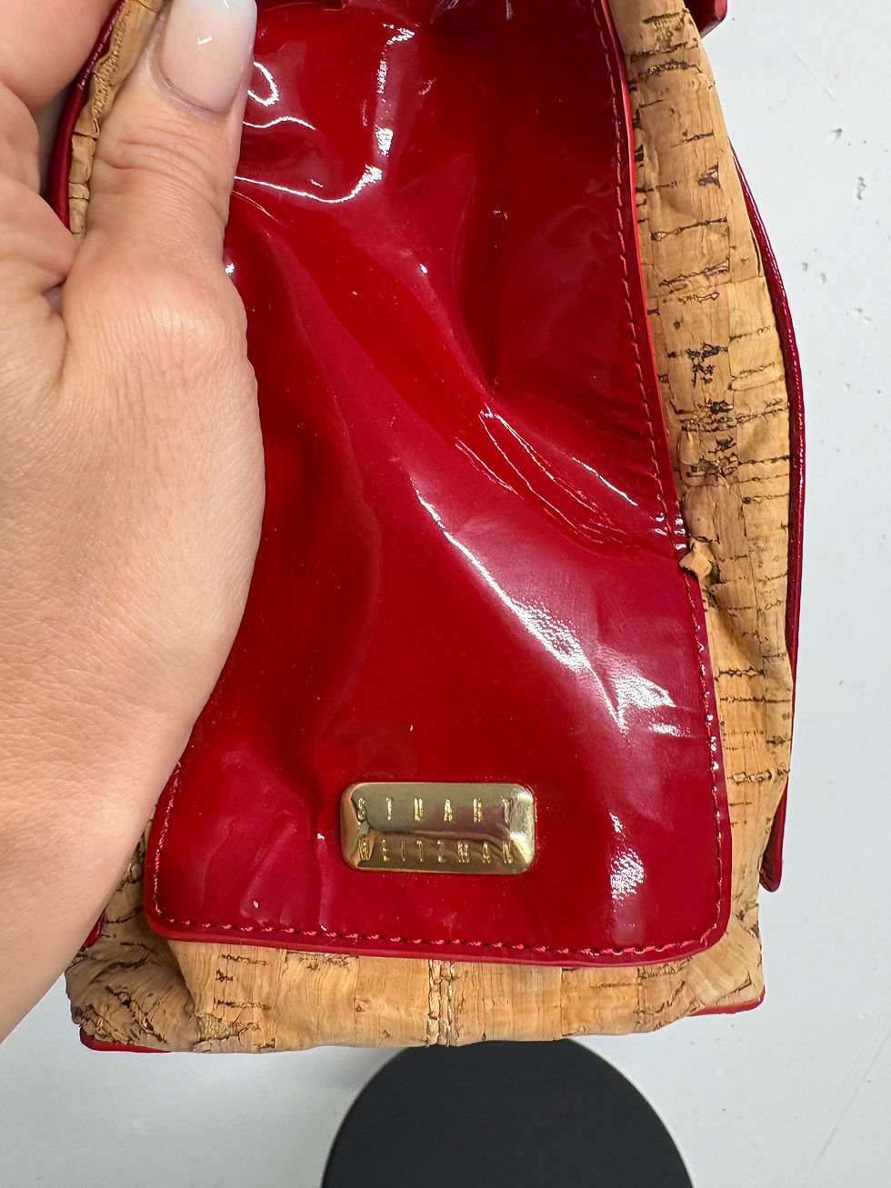 Miniaturbild: Hand hält rote Stuart Weitzman Handtasche mit Kork und goldenem Etikett.