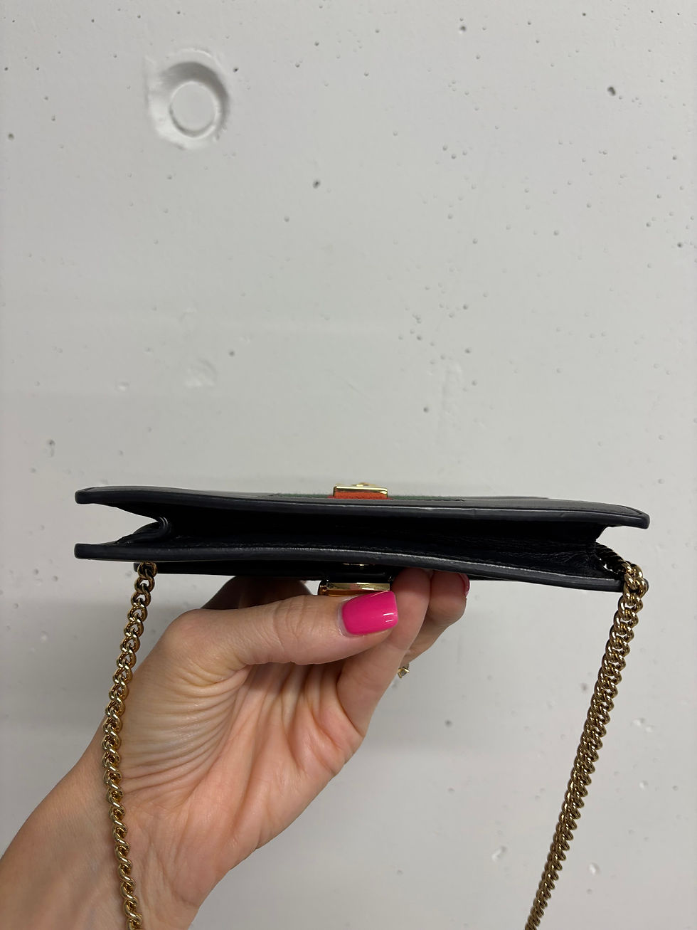 Miniaturbild: Schwarze Handtasche mit goldener Kette, gehalten von einer Person.