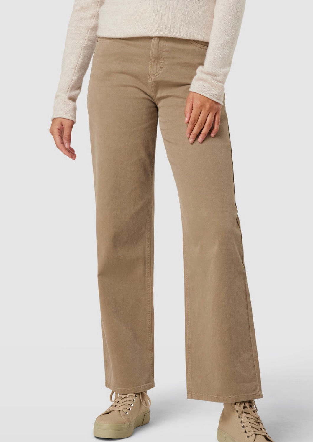 Eine Frau trägt hellbraune Hose in einem Studio vor weissem Hintergrund