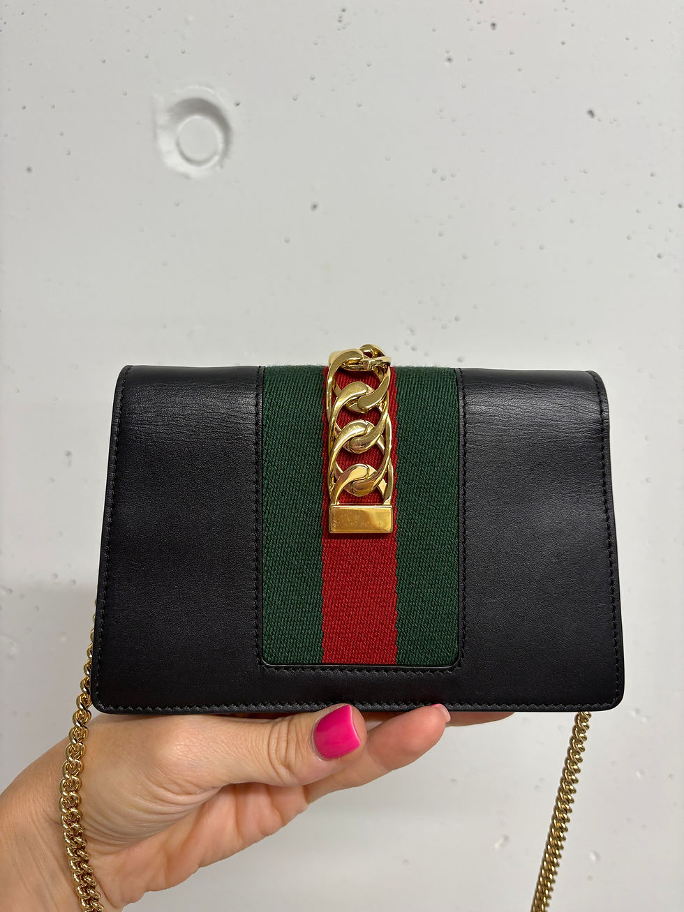 Miniaturbild: Schwarze Gucci-Tasche mit grünen und roten Streifen, goldener Kette, gehalten.