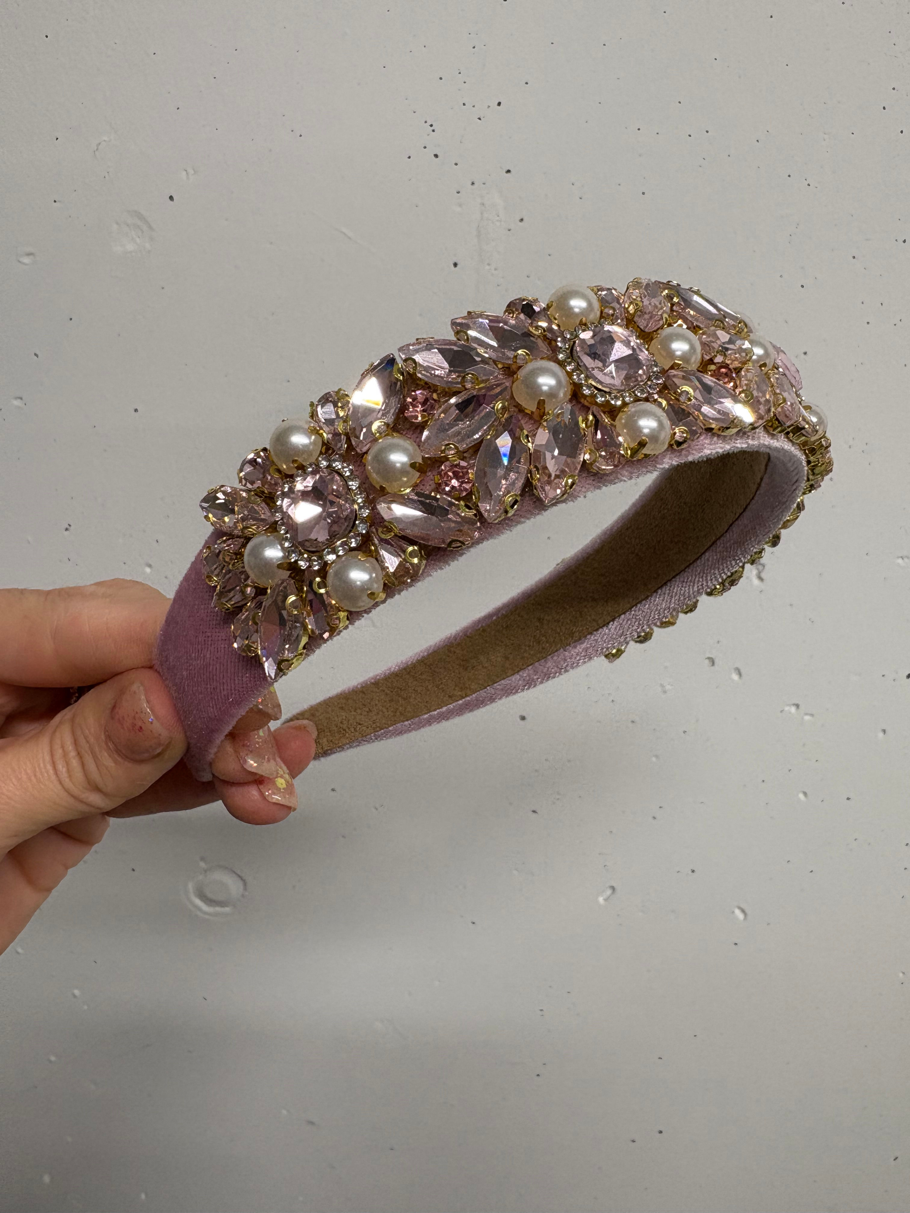 Hand holding a jeweled headband with pink crystals and pearls, elegant design.