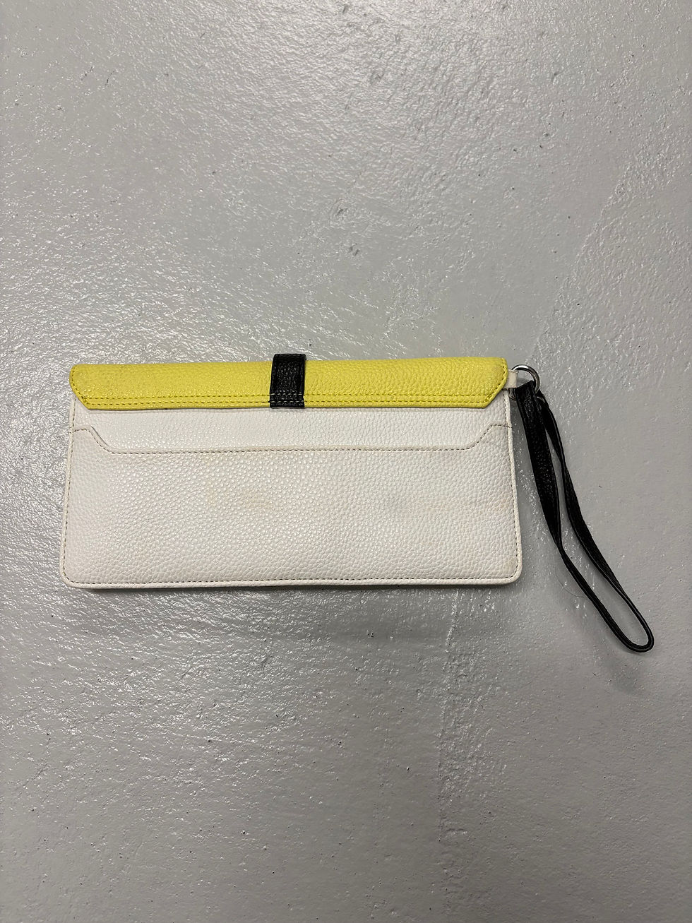 Miniaturbild: Gelb-weiße Handtasche mit schwarzem Riemen, auf grauem Untergrund, Detailaufnahme