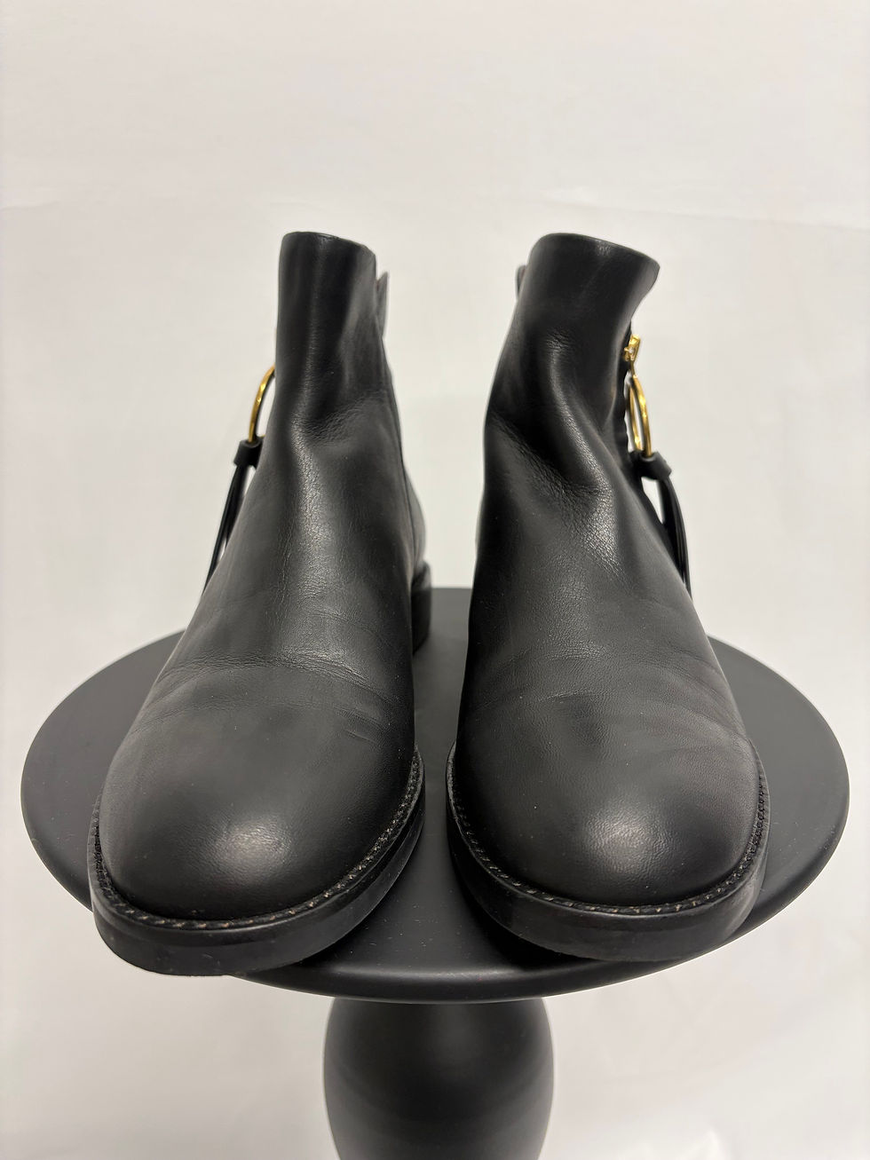 Miniaturbild: Schwarze Lederstiefel, Nahaufnahme, goldenen Schnallen, auf einem schwarzen Podest, Modeaccessoire.