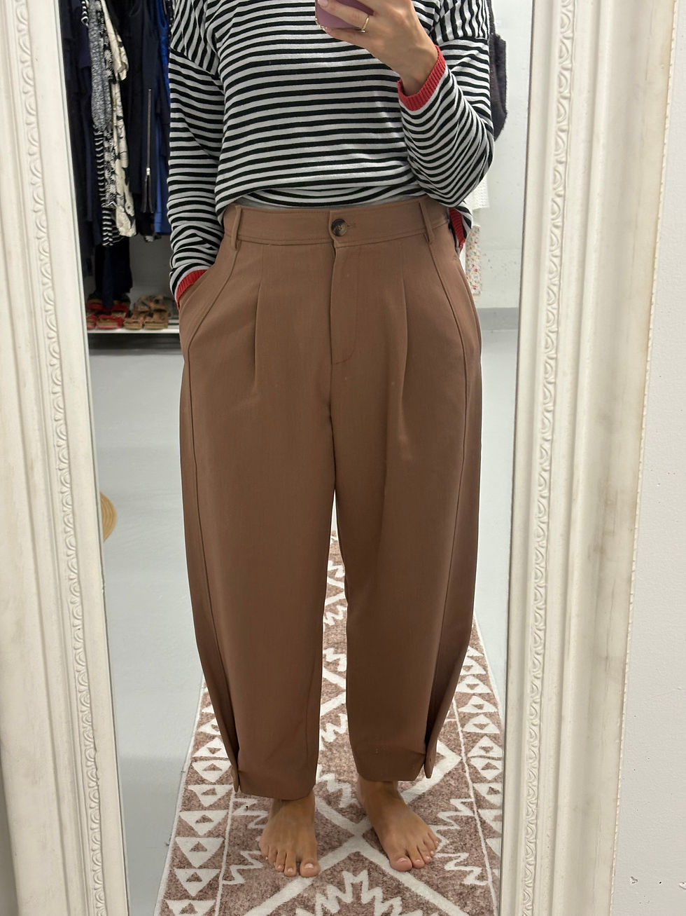 Frau trägt braune Hose, ein gestreiftes Shirt vor dem Spiegel. Kleidung im Spiegel