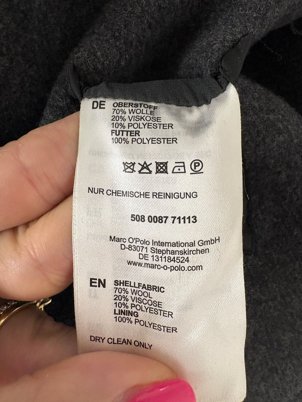 Miniaturbild: Kleidungsetikett mit Text: 70% Wolle, 20% Viskose, 10% Polyester, Nur chemische Reinigung.