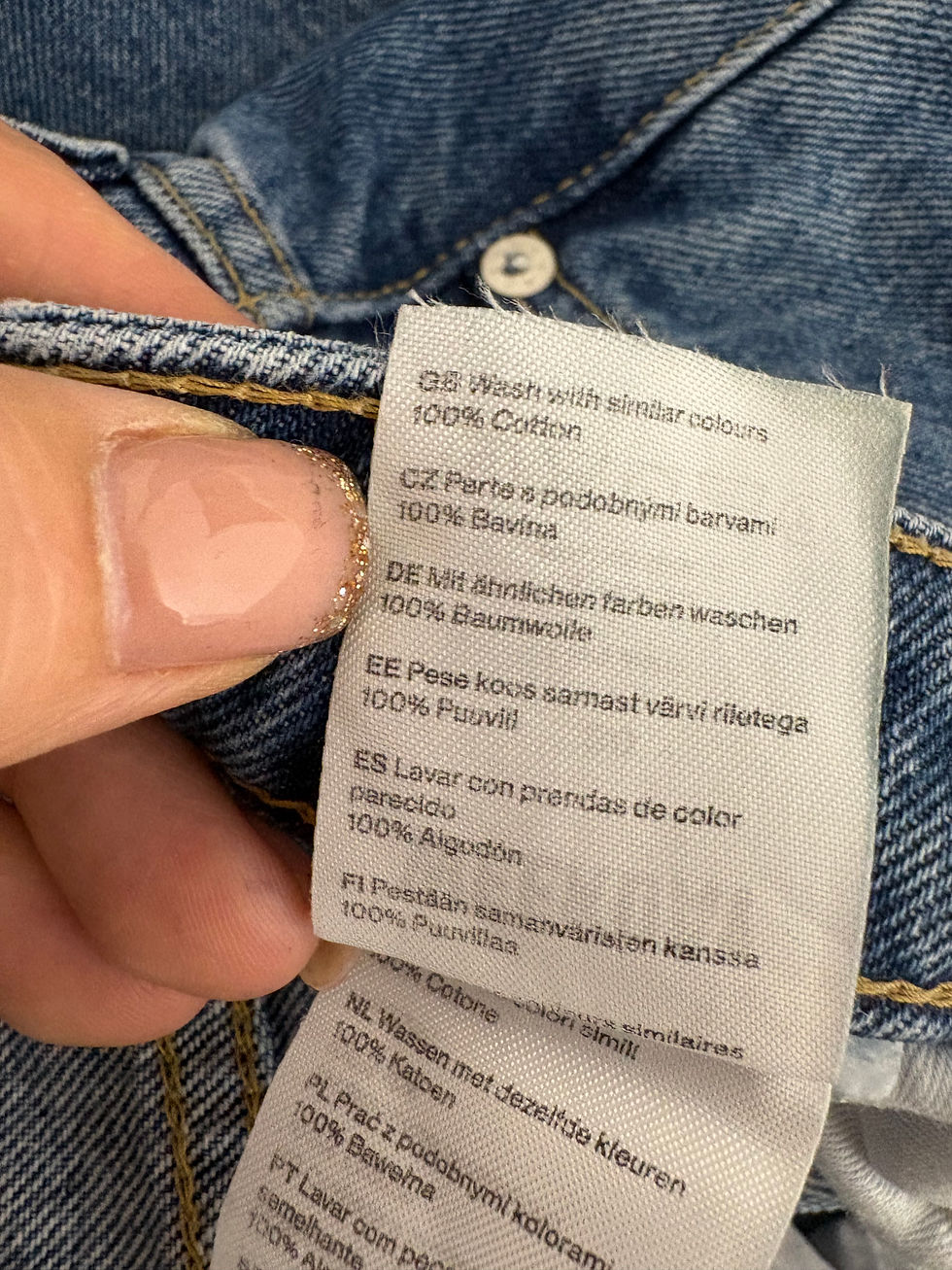 Miniaturbild: Hand holding jeans tag with text: Wash with similar colors, 100% Cotton.