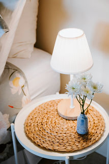White lamp and flowers on a bedside table in a bedroom.