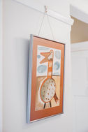 A framed art print hangs on a white wall; colorful bird illustration.